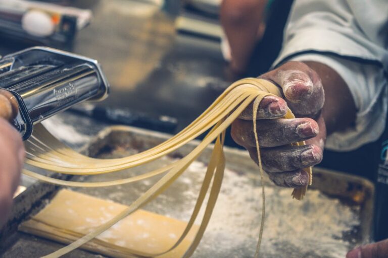 Hands cutting fresh tagliatelle on a flour-dusted wooden board