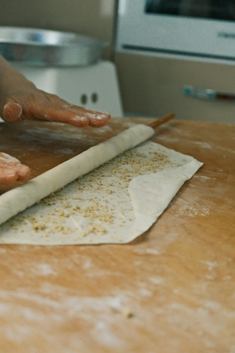 Hand rolling fresh pasta dough on a wooden surface